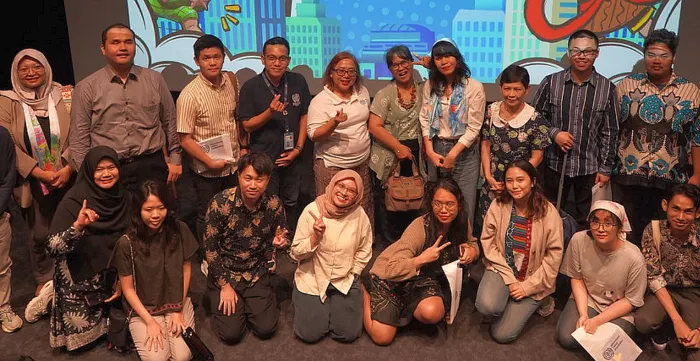 A group photo of participants and panelists in front of the stage.