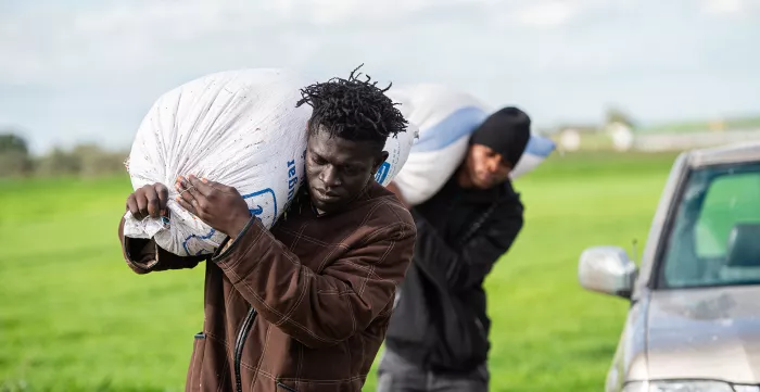 Two migrant workers carry heavy loads on their back