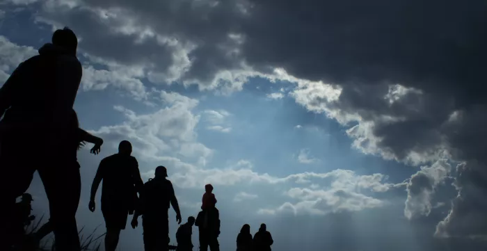 Sun rays illuminate people. Immigration of people. Blue sky with dark clouds.
